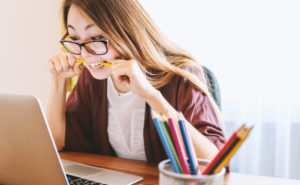 girl looking at laptop biting a pencil