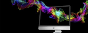 A computer monitor with a sleek design set against a black background. Vibrant, multicolored waves of light appear to flow out of the screen, creating a dynamic and creative visual effect.