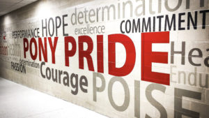 A school hallway mural featuring the words "PONY PRIDE" in bold red, surrounded by motivational words like "Courage," "Hope," "Commitment," and "Determination" in various sizes and neutral tones.
