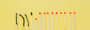 A row of matches on a yellow background, with several burned and blackened matches on the left and unlit red-tipped matches on the right.