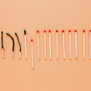 A row of matches on an orange background, with several burned and blackened matches on the left and unlit red-tipped matches on the right.