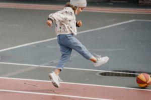A child kicking a ball outside on a paved ground.
