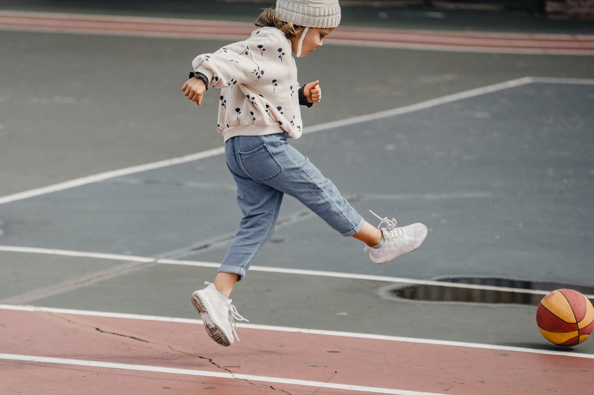 A child kicking a ball outside on a paved ground.