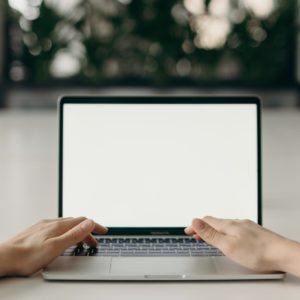 hands typing on a laptop keyboard with a blank screen