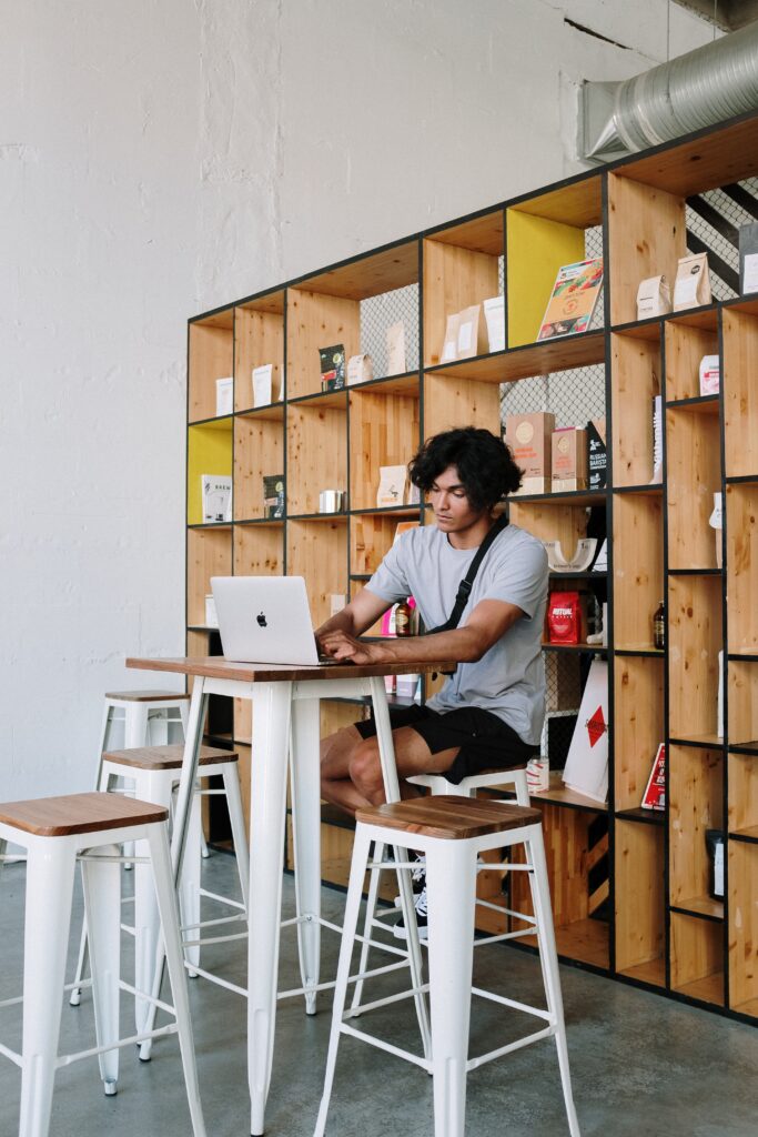 A person sits at a high-top table working on a laptop with bookshelves behind them