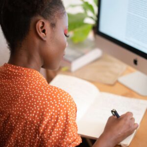 Person sitting at computer writing in a notebook