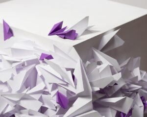White paper airplanes in a pile with a few interspersed purple paper airplanes. Implies change being tossed around.