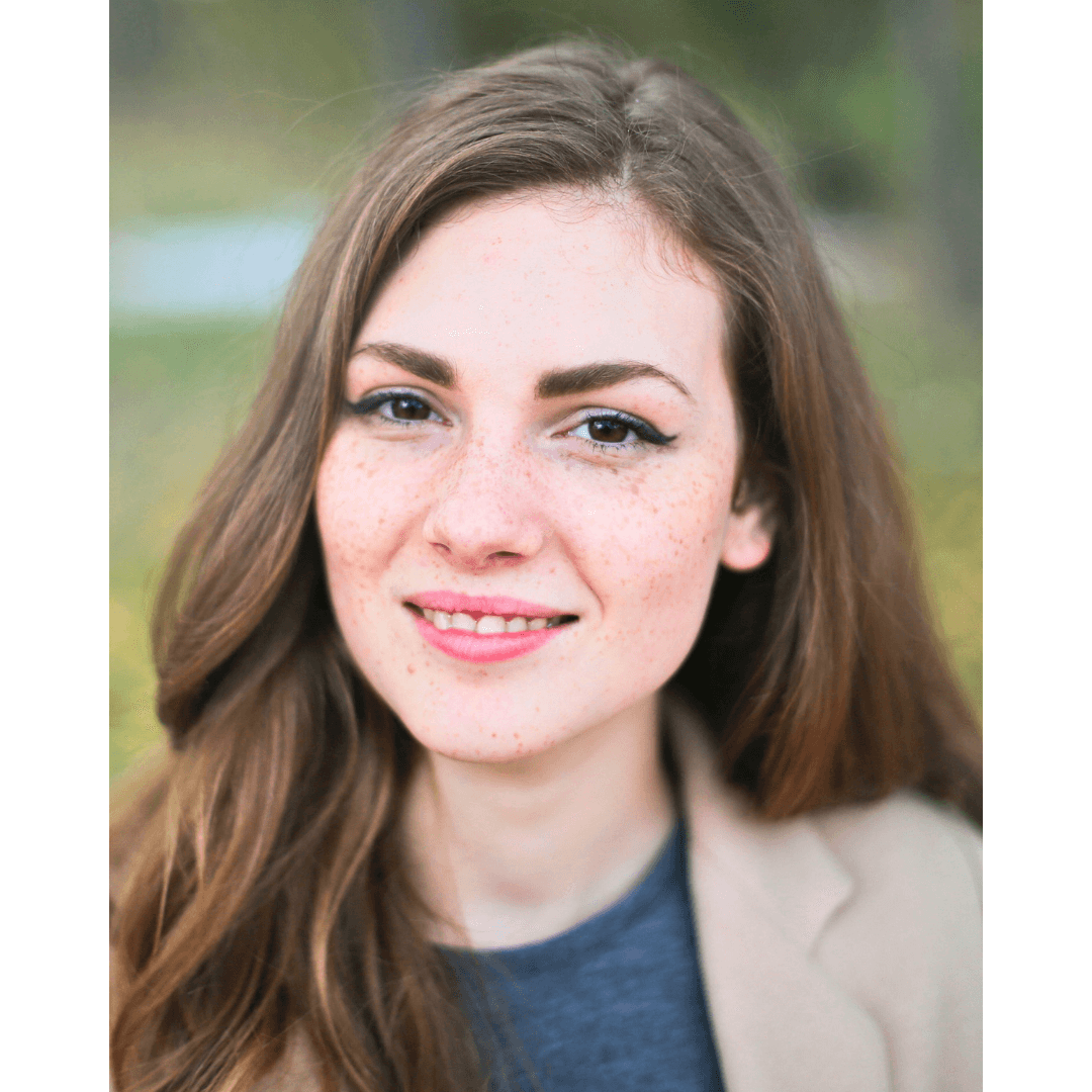 Headshot of a woman with freckles, against a natural background