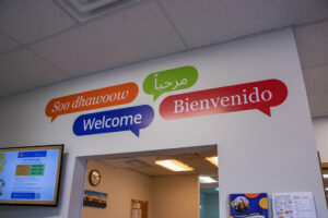 Welcome in english, spanish, arabic, and english in speech bubbles on a wall