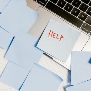 A laptop with a blue sticky note on the keyboard that says "Help!" in red marker